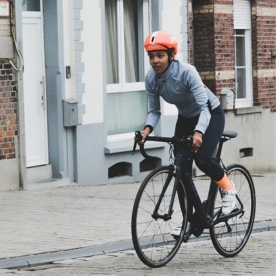 a female biker with a grey sweater and red helmet biking next to a brick house